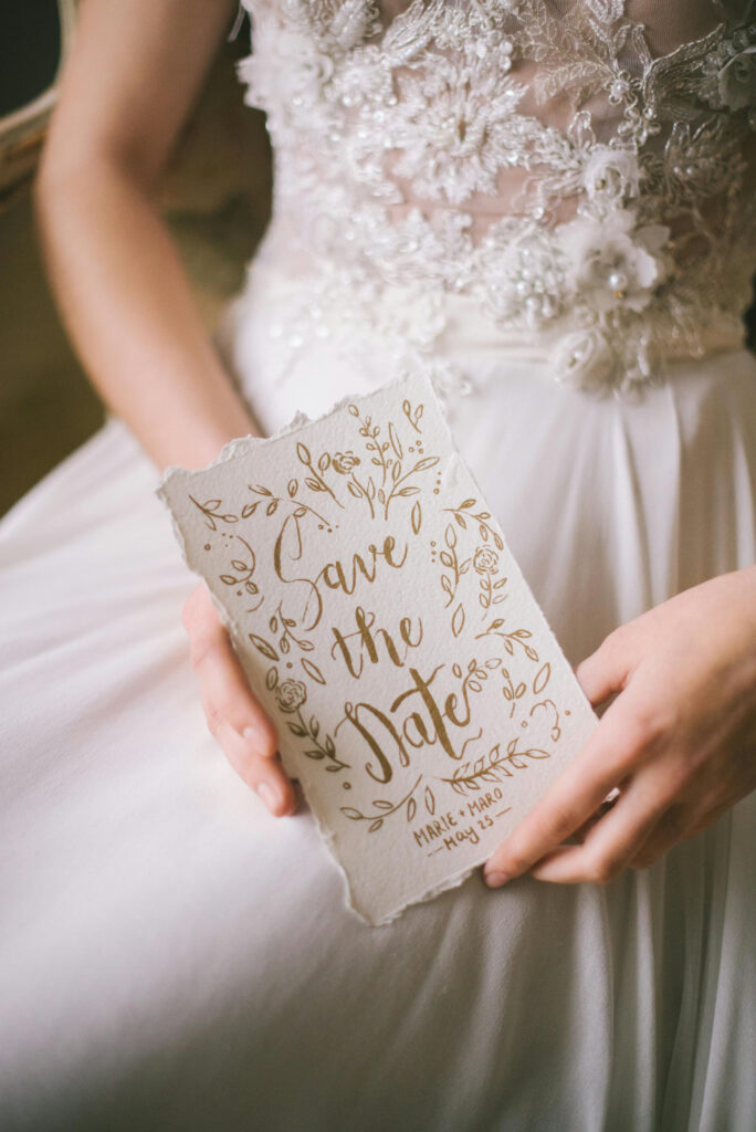 Hand holding elegant save the date card for destination wedding, highlighting the wedding date details.