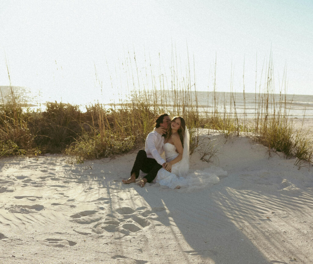 Bride and groom sitting barefoot in the sand while planning a destination wedding on a beach.